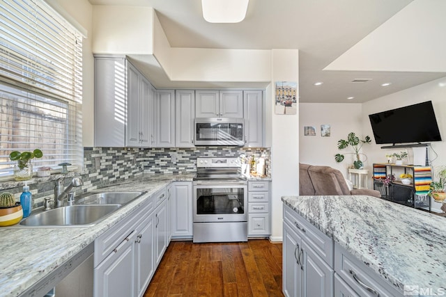 kitchen featuring stainless steel appliances, tasteful backsplash, dark wood-type flooring, a sink, and light stone countertops