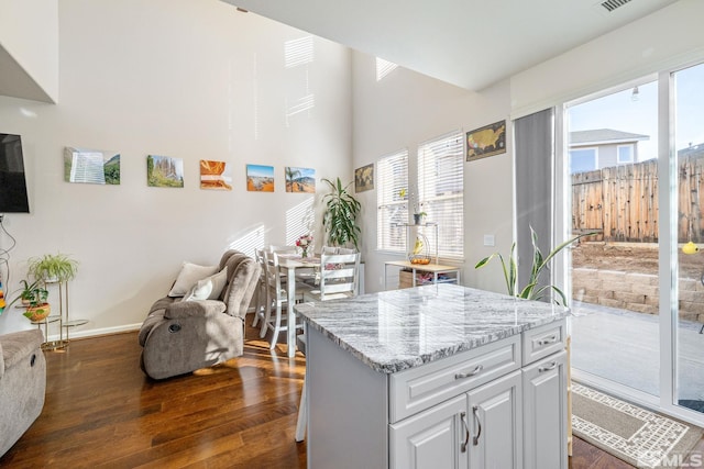 kitchen featuring a kitchen island, open floor plan, dark wood-style flooring, light stone countertops, and white cabinetry