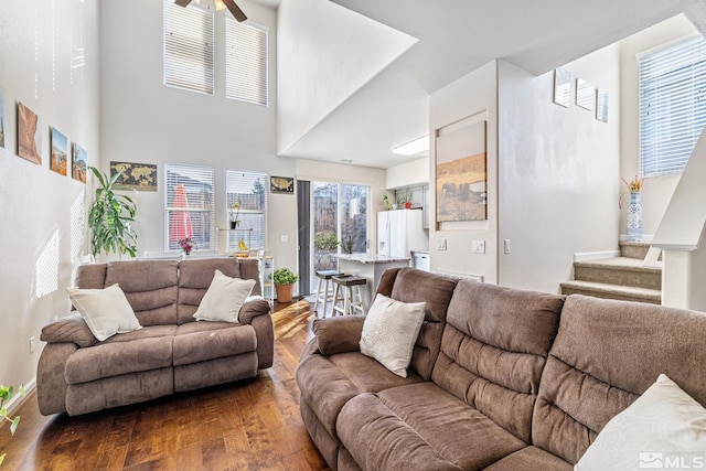 living room with a towering ceiling, ceiling fan, and dark wood finished floors