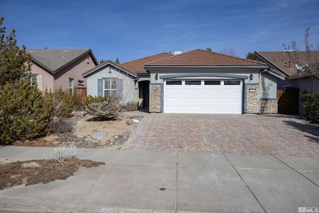 ranch-style house featuring decorative driveway, a tile roof, stucco siding, an attached garage, and stone siding