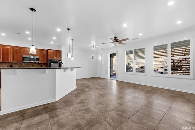 kitchen featuring brown cabinets, stainless steel microwave, hanging light fixtures, oven, and a kitchen breakfast bar