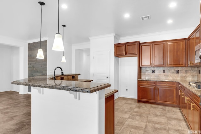 kitchen featuring brown cabinetry, decorative backsplash, a kitchen breakfast bar, hanging light fixtures, and a peninsula