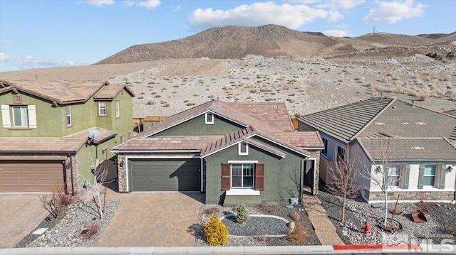 view of front of house with decorative driveway, a mountain view, an attached garage, and stucco siding