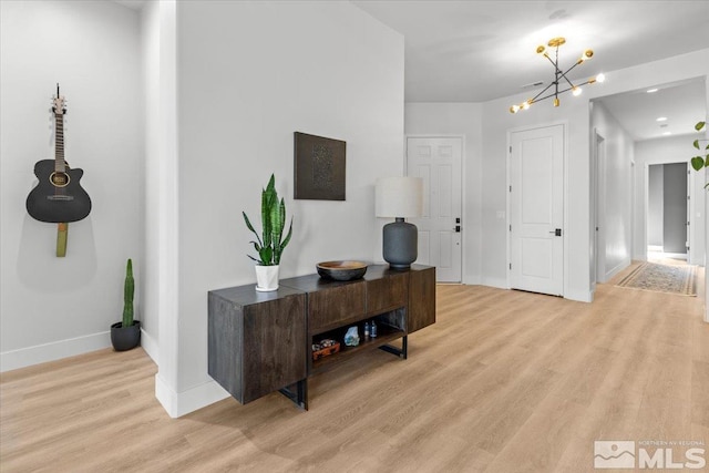 interior space featuring light wood-style flooring, baseboards, and an inviting chandelier