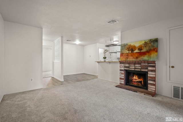 unfurnished living room featuring a brick fireplace, a textured ceiling, visible vents, and carpet flooring