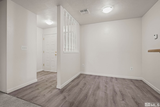 spare room with a textured ceiling, light wood-style flooring, visible vents, and baseboards