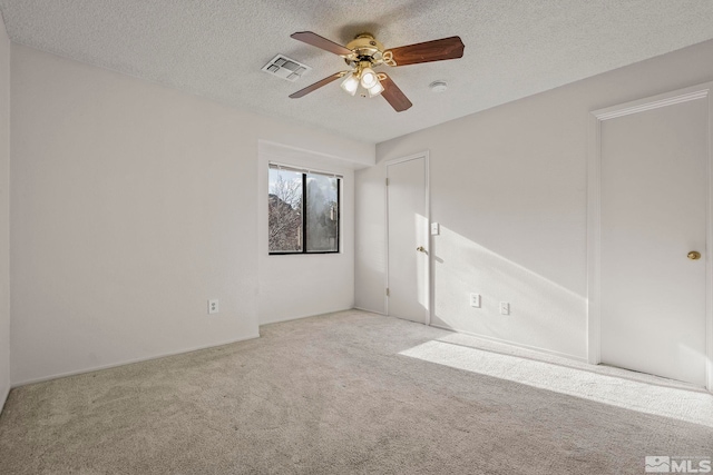 empty room with a textured ceiling, ceiling fan, visible vents, and light colored carpet