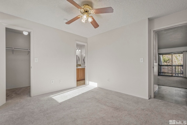 unfurnished bedroom featuring light colored carpet, ceiling fan, a spacious closet, and a textured ceiling