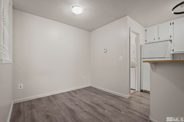 unfurnished dining area featuring light wood-style floors, a textured ceiling, and baseboards