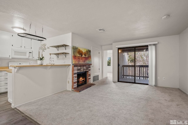 unfurnished living room featuring light carpet, a fireplace, visible vents, and a textured ceiling