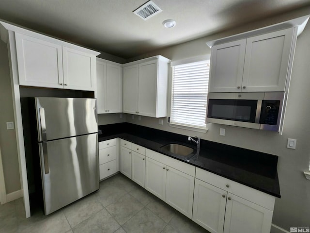 kitchen with stainless steel appliances, dark countertops, a sink, and white cabinets