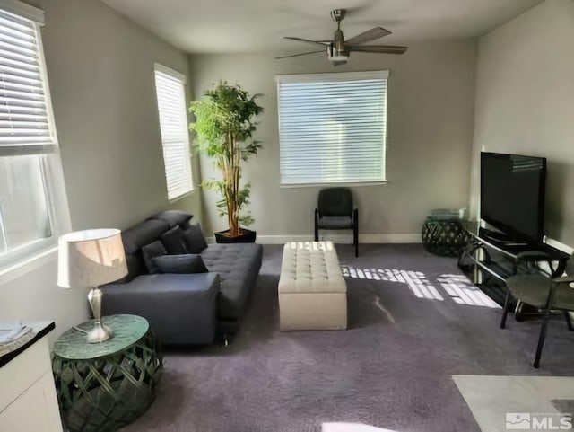 living area with baseboards, dark carpet, and a ceiling fan