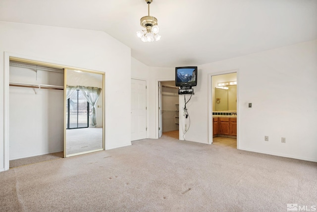 unfurnished bedroom featuring light carpet, connected bathroom, lofted ceiling, a chandelier, and multiple closets