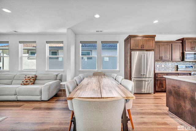 kitchen featuring light wood-style flooring, stainless steel appliances, open floor plan, light countertops, and backsplash