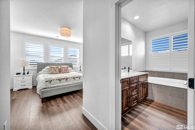 ensuite bathroom with connected bathroom, wood finished floors, vanity, baseboards, and a bath