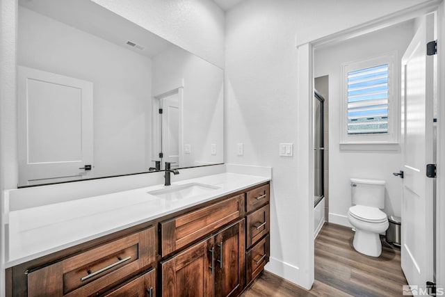 bathroom with shower / bath combination with glass door, visible vents, toilet, vanity, and wood finished floors