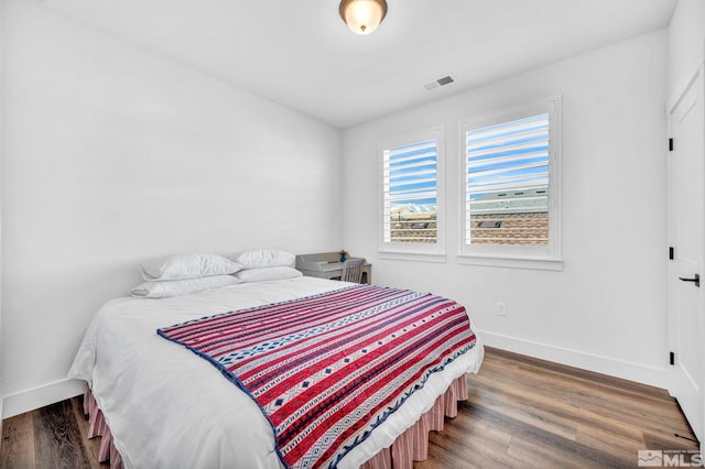 bedroom with dark wood-style floors, visible vents, and baseboards