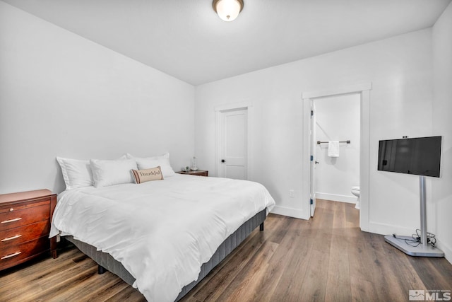 bedroom with ensuite bath, wood finished floors, and baseboards