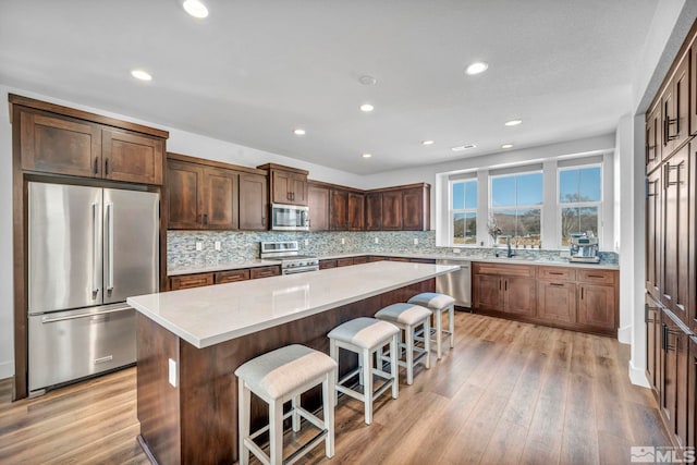 kitchen featuring a center island, a breakfast bar, light countertops, appliances with stainless steel finishes, and light wood-style floors