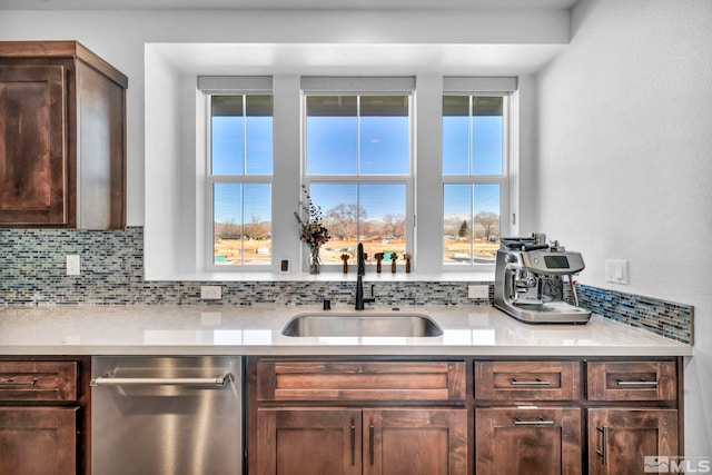 kitchen featuring a sink, light countertops, stainless steel dishwasher, dark brown cabinets, and tasteful backsplash