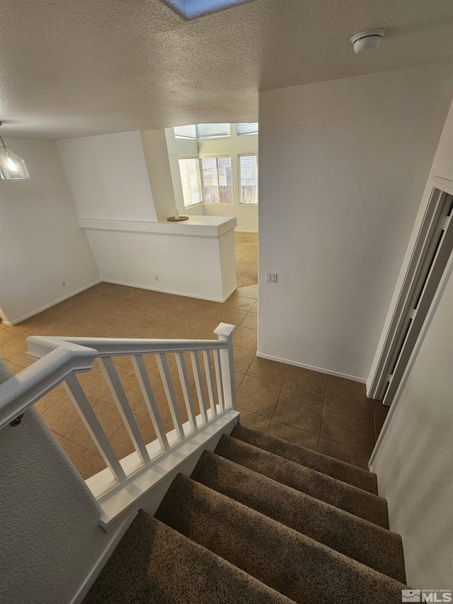 stairway with baseboards, a textured ceiling, and tile patterned floors