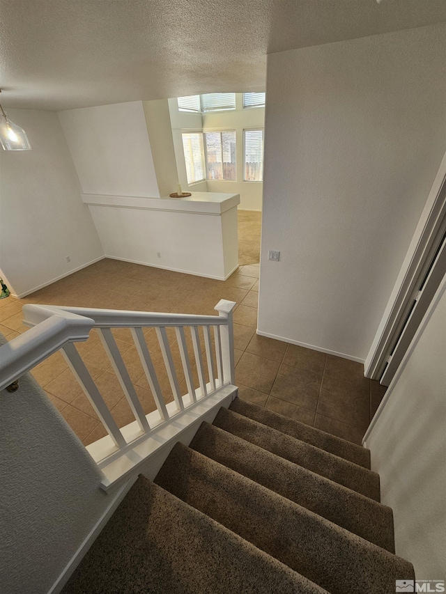 stairs with tile patterned flooring, baseboards, and a textured ceiling