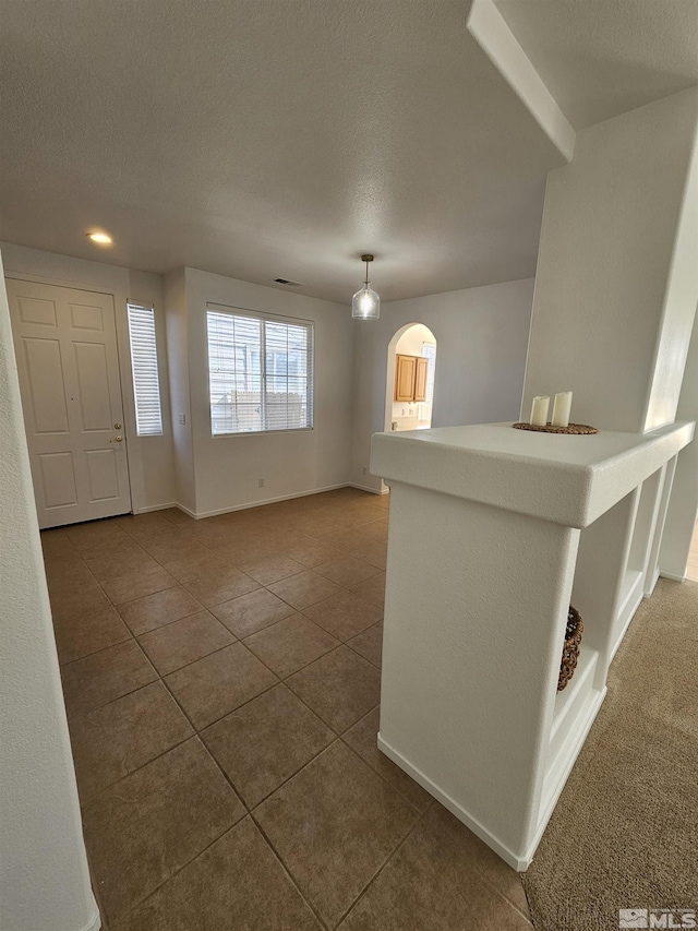 tiled foyer featuring arched walkways, visible vents, a textured ceiling, and baseboards