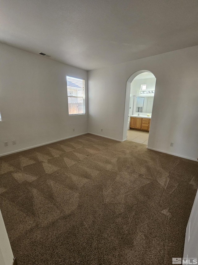 spare room with arched walkways, light colored carpet, visible vents, and baseboards