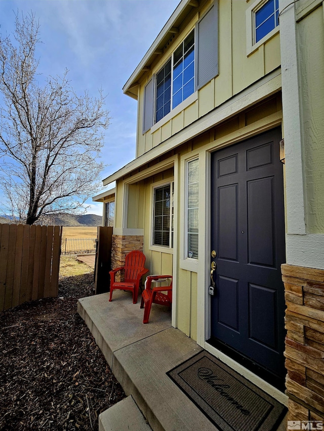 view of exterior entry with stone siding, board and batten siding, and fence