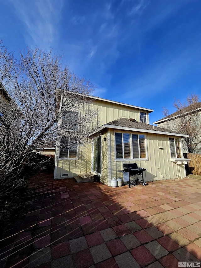 rear view of house featuring a patio, a shingled roof, and board and batten siding