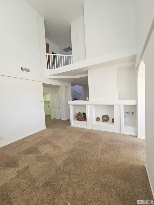 unfurnished living room featuring carpet, a high ceiling, visible vents, and baseboards