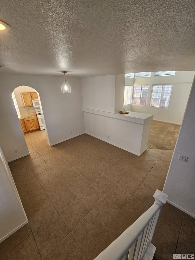 tiled empty room featuring arched walkways, a textured ceiling, and baseboards