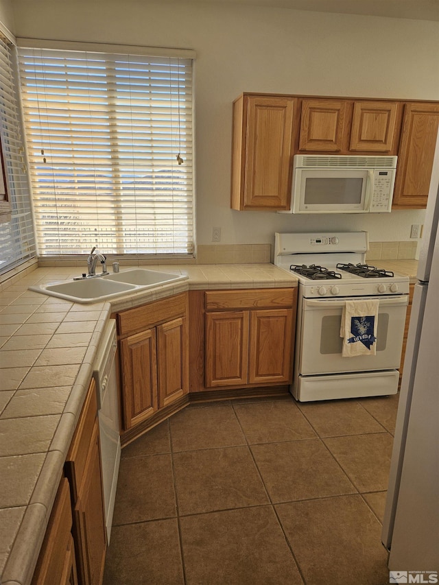 kitchen with white appliances, dark tile patterned floors, tile counters, and a sink