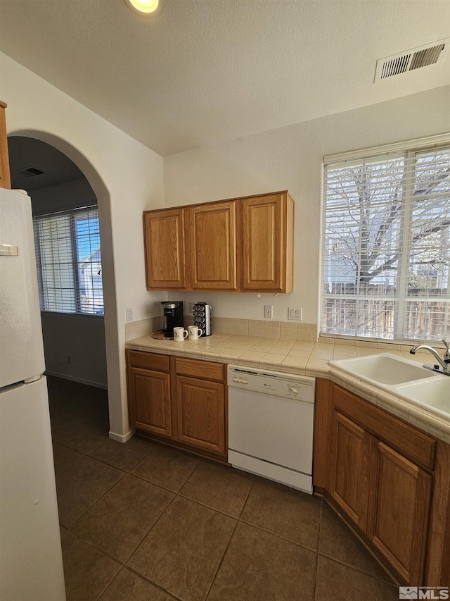 kitchen featuring white appliances, visible vents, arched walkways, light countertops, and a sink