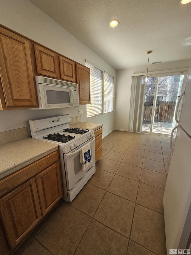 kitchen with light tile patterned floors, white appliances, tile counters, brown cabinets, and decorative light fixtures