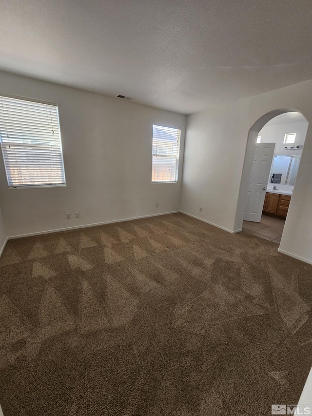 empty room featuring carpet floors, arched walkways, visible vents, a textured ceiling, and baseboards