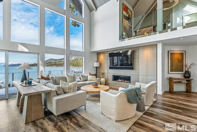 living area with a water view, wood finished floors, a towering ceiling, baseboards, and a glass covered fireplace