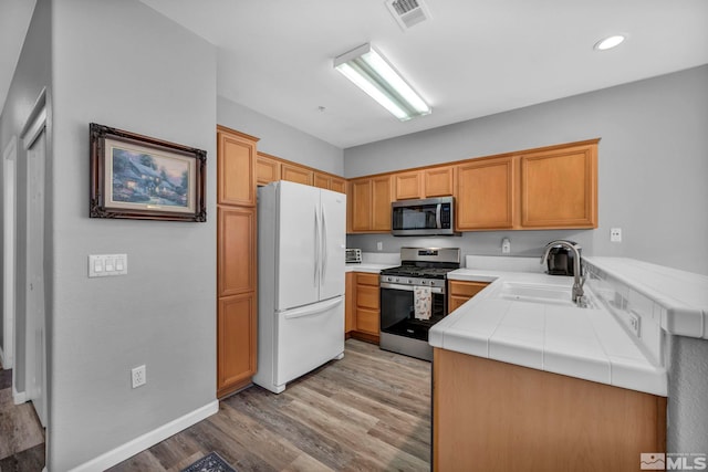 kitchen featuring tile countertops, light wood finished floors, appliances with stainless steel finishes, and a sink