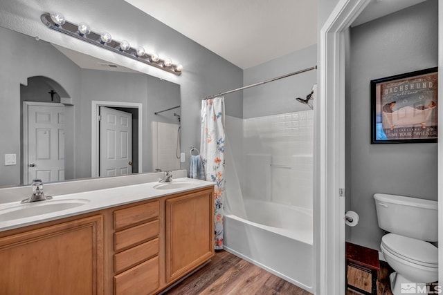 bathroom with toilet, wood finished floors, a sink, and shower / bath combo with shower curtain