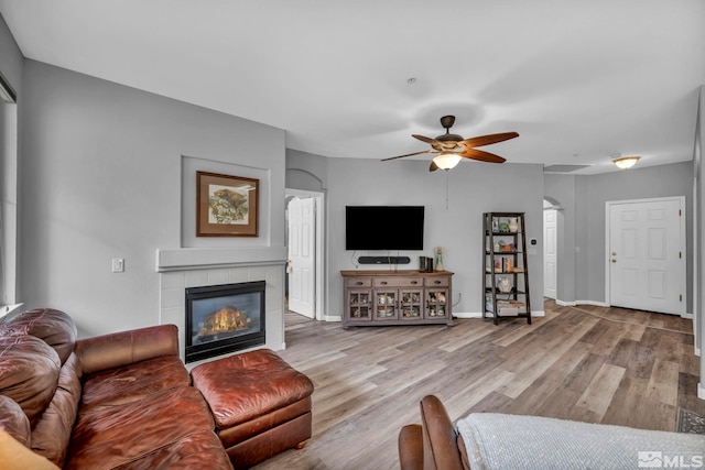 living area with light wood-style floors, a tile fireplace, baseboards, and a ceiling fan