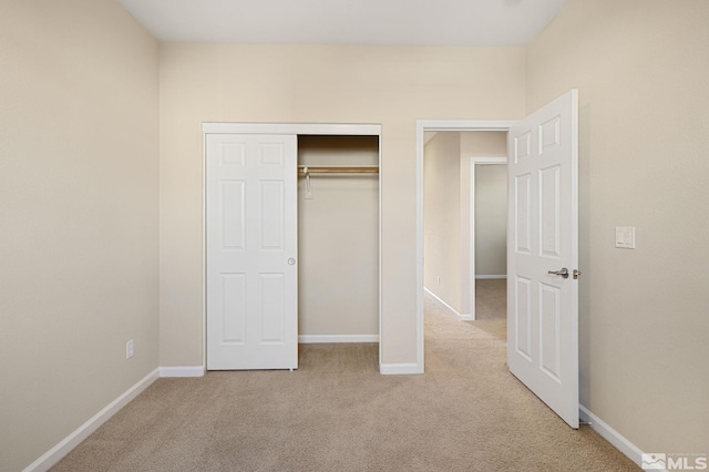 unfurnished bedroom featuring a closet, light carpet, and baseboards