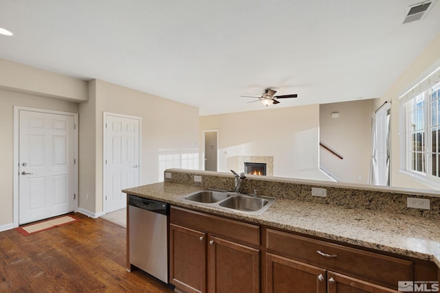 kitchen with visible vents, dark wood finished floors, a lit fireplace, stainless steel dishwasher, and a sink