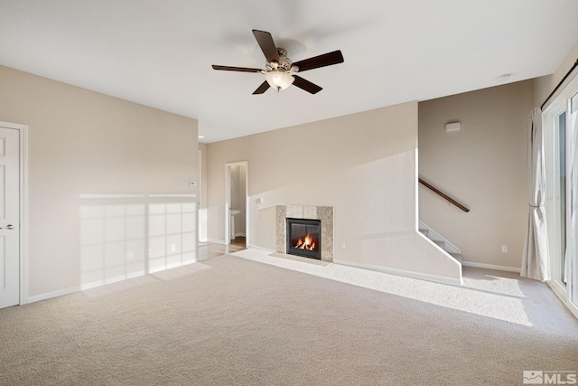 unfurnished living room with light colored carpet, a fireplace, a ceiling fan, baseboards, and stairs