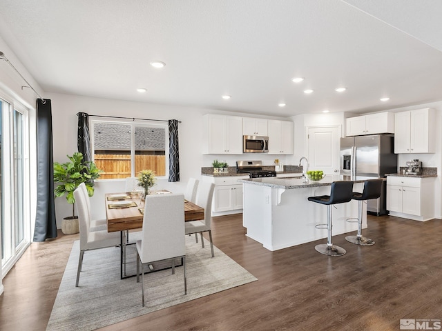 kitchen with stainless steel appliances, white cabinets, dark stone counters, plenty of natural light, and a center island with sink