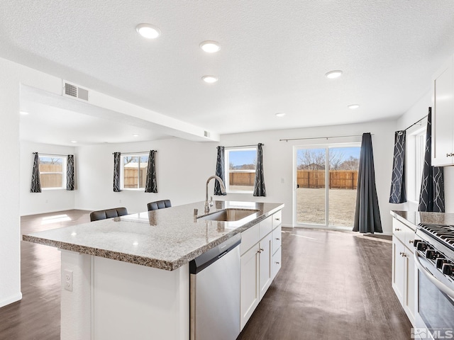 kitchen featuring stainless steel appliances, an island with sink, a sink, and white cabinets