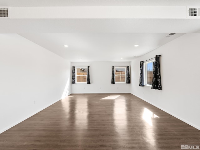 spare room with dark wood-type flooring, visible vents, and baseboards