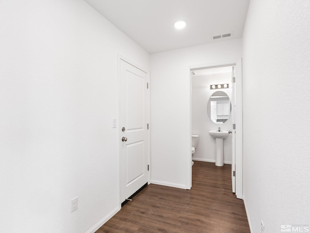 hall featuring dark wood-style flooring, visible vents, and baseboards