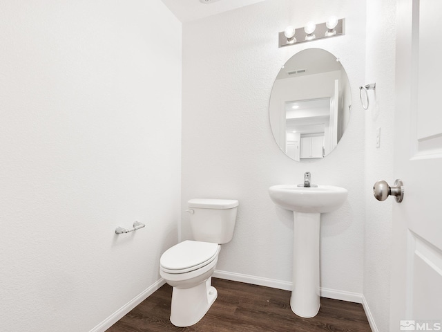 bathroom with toilet, visible vents, baseboards, and wood finished floors