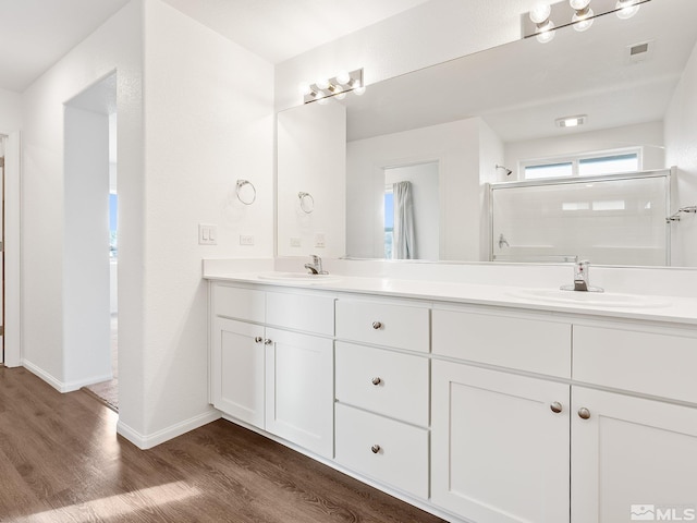 full bath featuring double vanity, wood finished floors, a sink, and visible vents