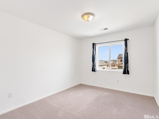 carpeted spare room featuring a textured ceiling, visible vents, and baseboards